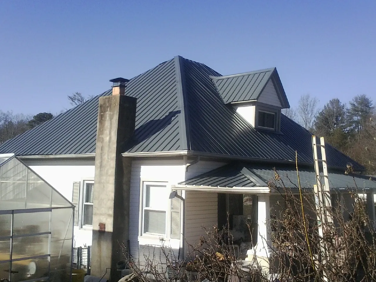 Dark blue standing seam metal roof on a white farmhouse with dormer — Slate & Tile Roof Repair by Roofing Brothers in Toney