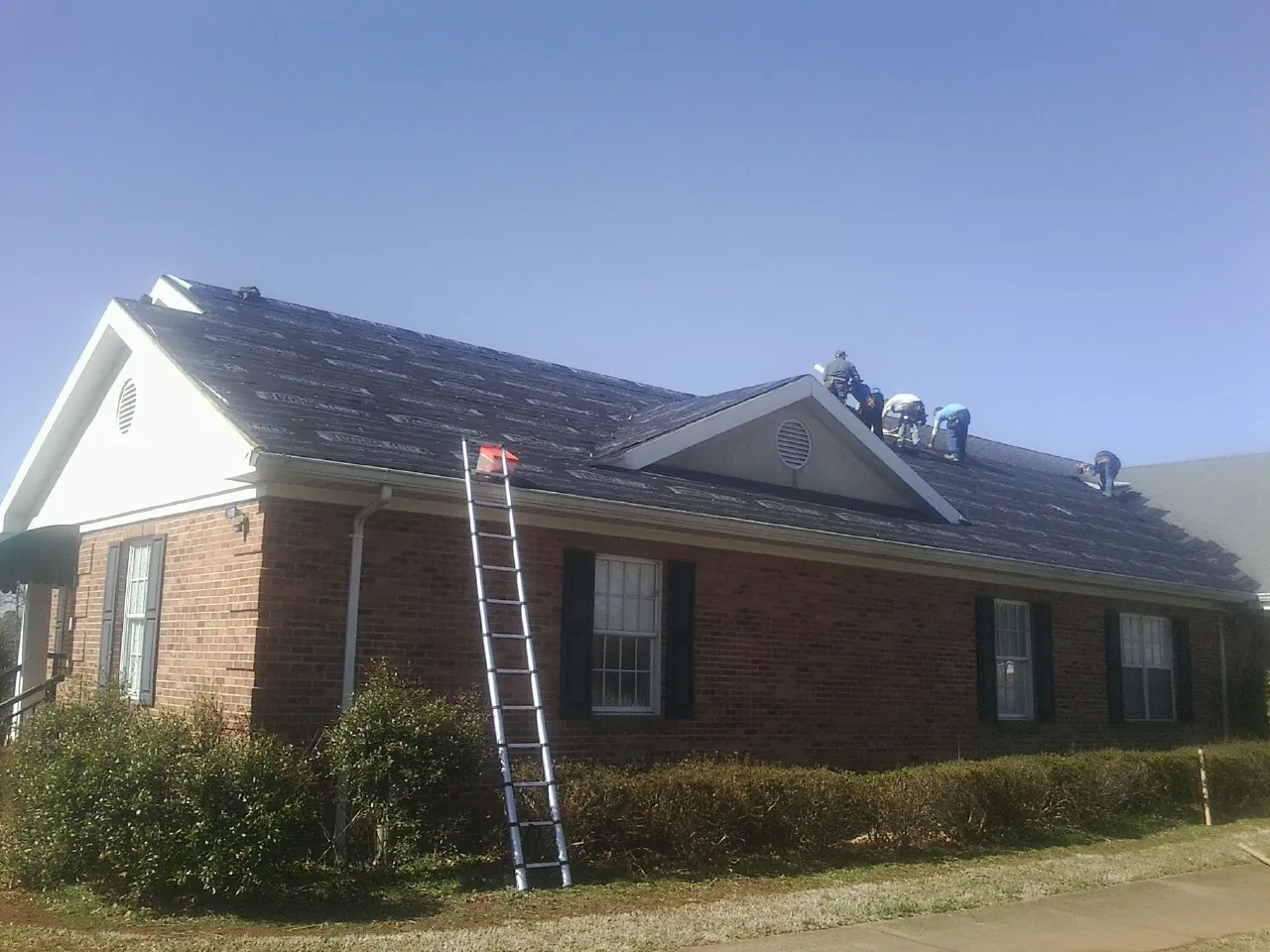 Crew tearing shingles off a brick ranch roof with a ladder set — Emergency Roof Repair work by our crew in Toney