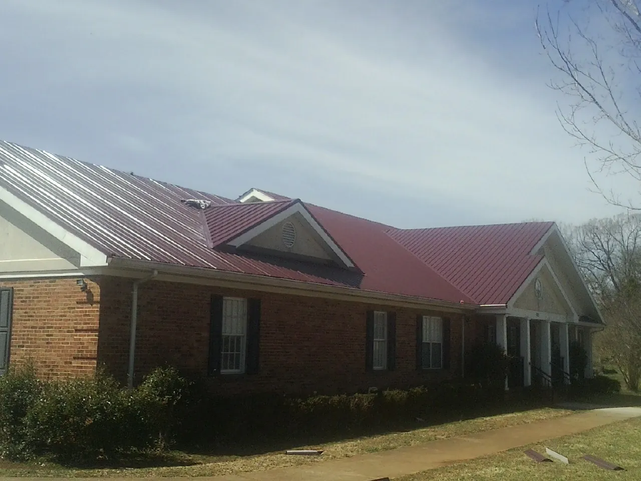 Red metal roof with gabled entries on a long brick building, from a Hail Damage Roof Repair job in Toney