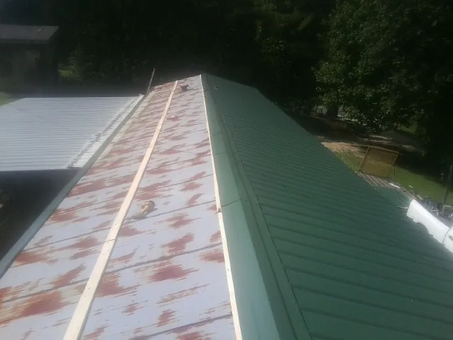 Old rusted panels beside newly installed green metal roofing — Wind Damage Roof Repair by Roofing Brothers in Toney
