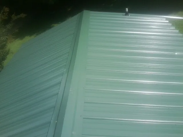 New green metal panels meeting at the ridge of a roof — Flat Roof Repair work by our crew in Toney