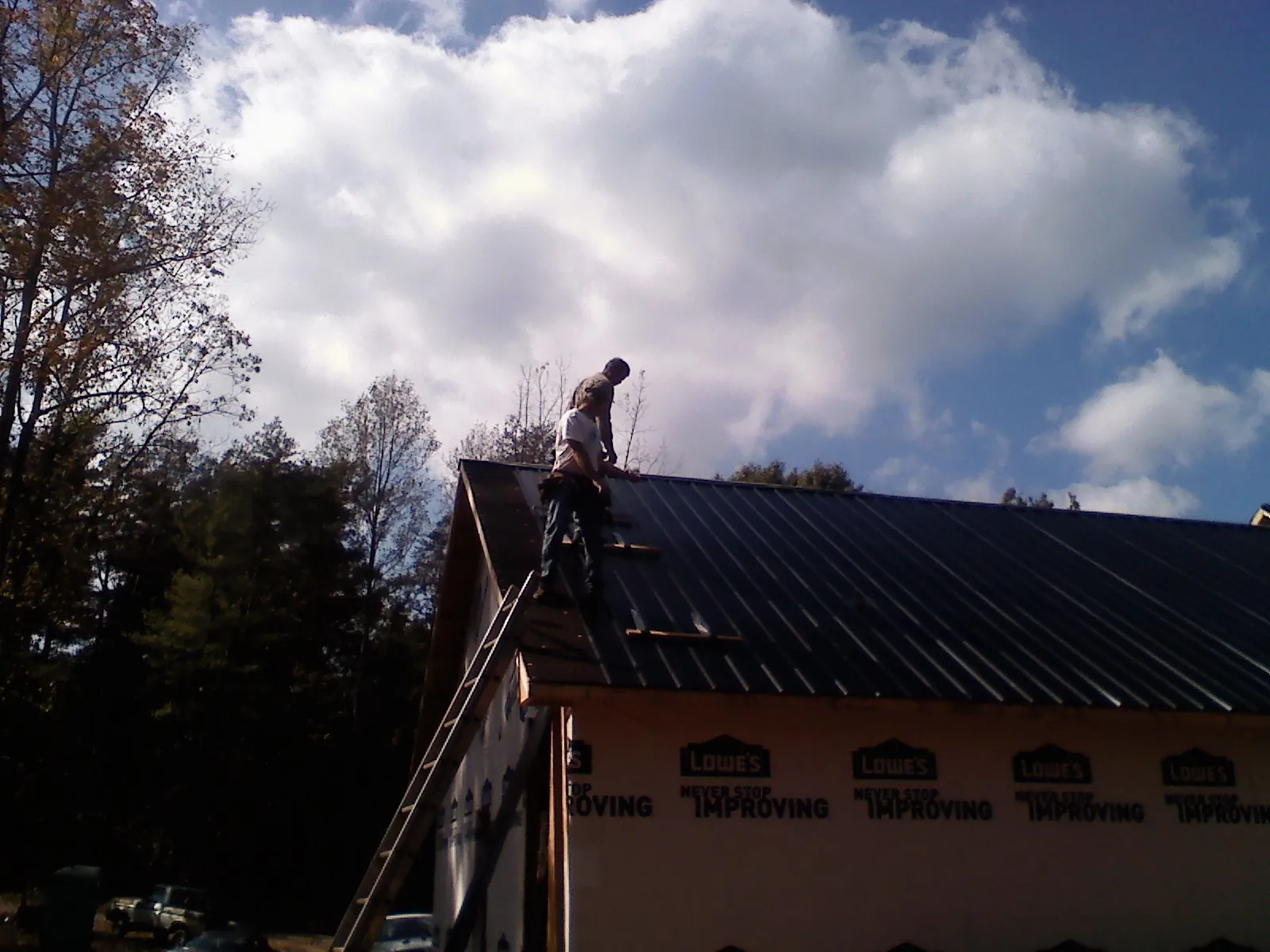 Roofer fastening dark metal panels high against a cloudy sky, from a Roof Inspection job in Toney