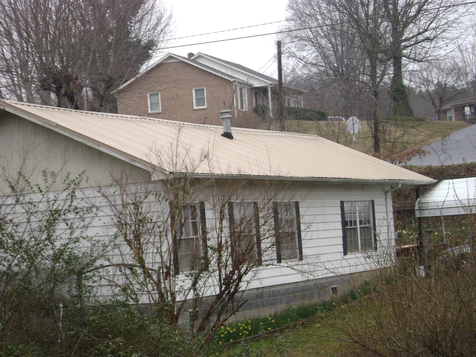 Tan metal roof on a white sided house set into a hillside — Commercial Roofing by Roofing Brothers in Toney