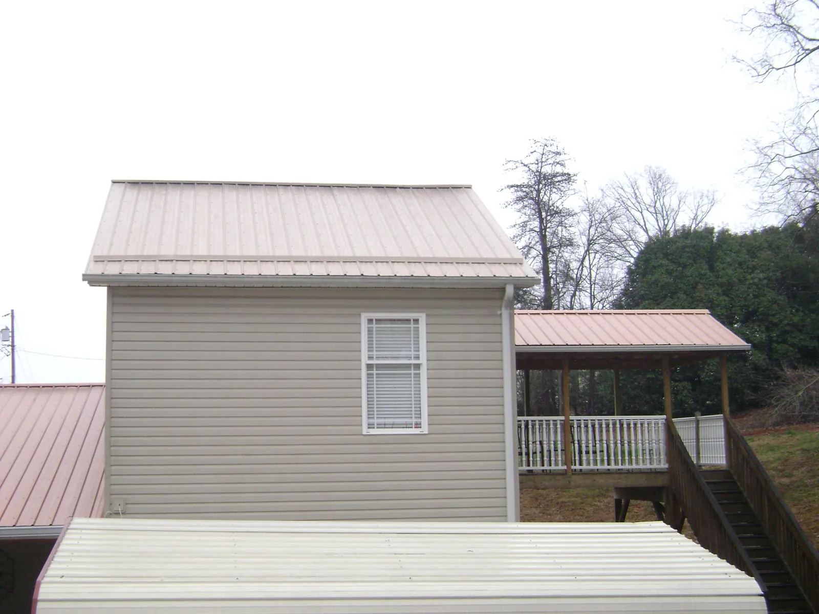 Tan metal roofs on a two story addition and attached porch, from a Roof Replacement job in Toney