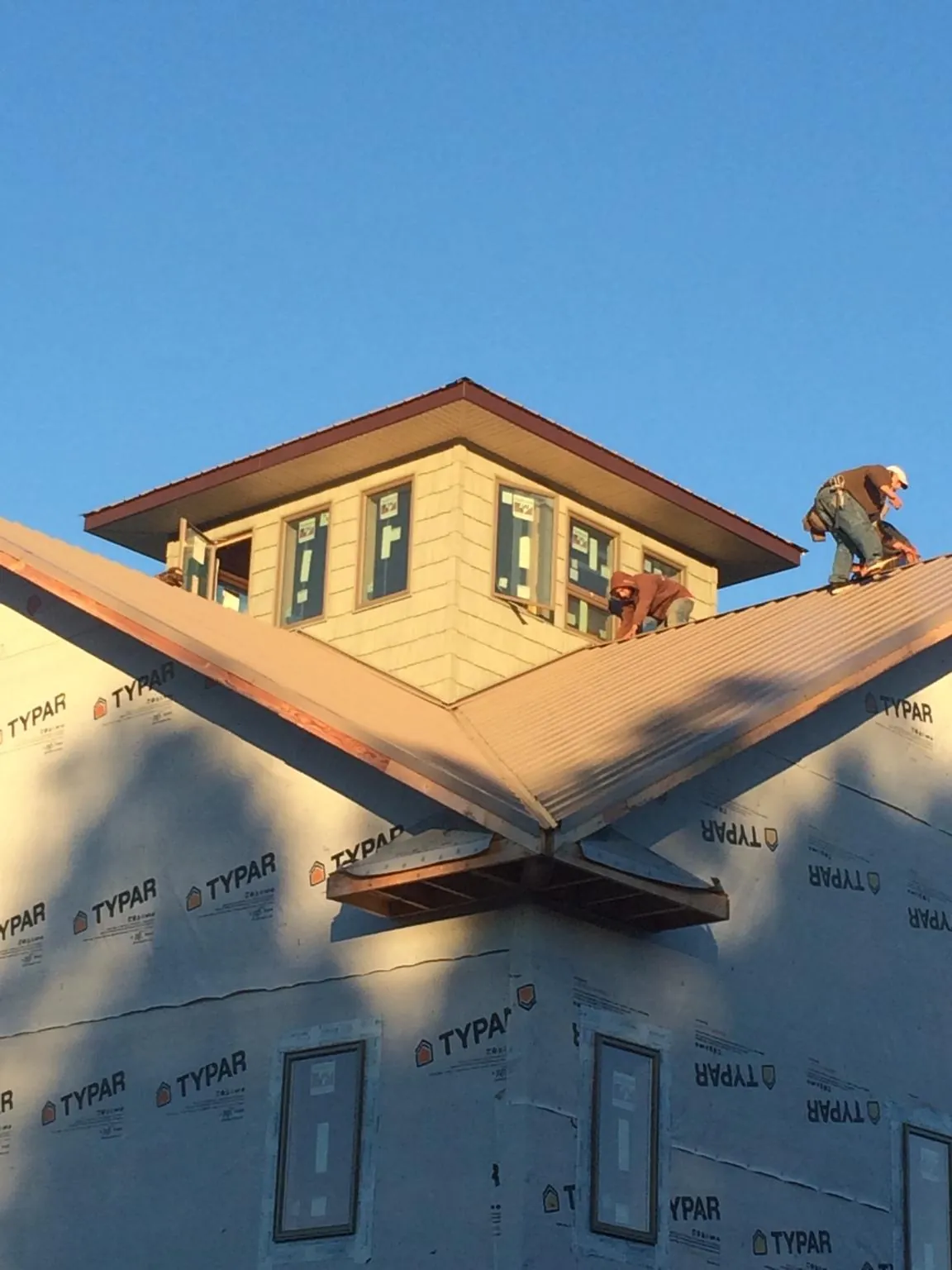 Roofers working around a rooftop cupola on a new metal roof at sunset in Toney